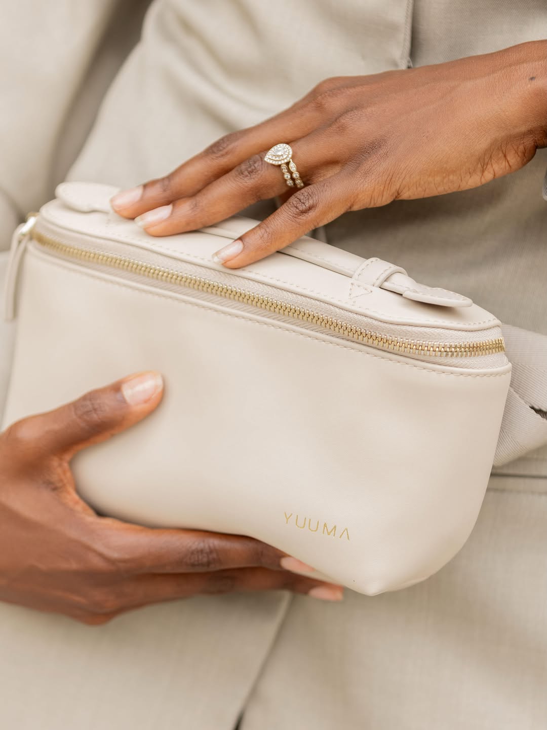 Hands holding the ivory YUUMA Jolie belt bag with gold zipper